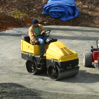 worker drives a compactor over crushed stone